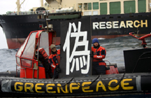 グリーンピースが用意した看板のバックが調査捕鯨「日新丸」、日本の調査捕鯨は「偽」の科学調査だとNHKは伝えている